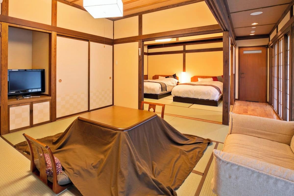 A traditional Japanese-style room with tatami flooring, a television, a desk, and a bed with a view of the outside.