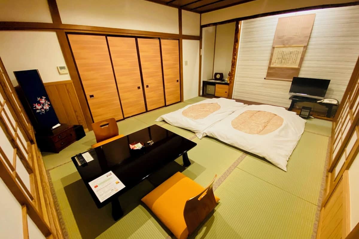 A traditional Japanese room with tatami flooring, a futon bed, a low table, a television, and a cabinet.
