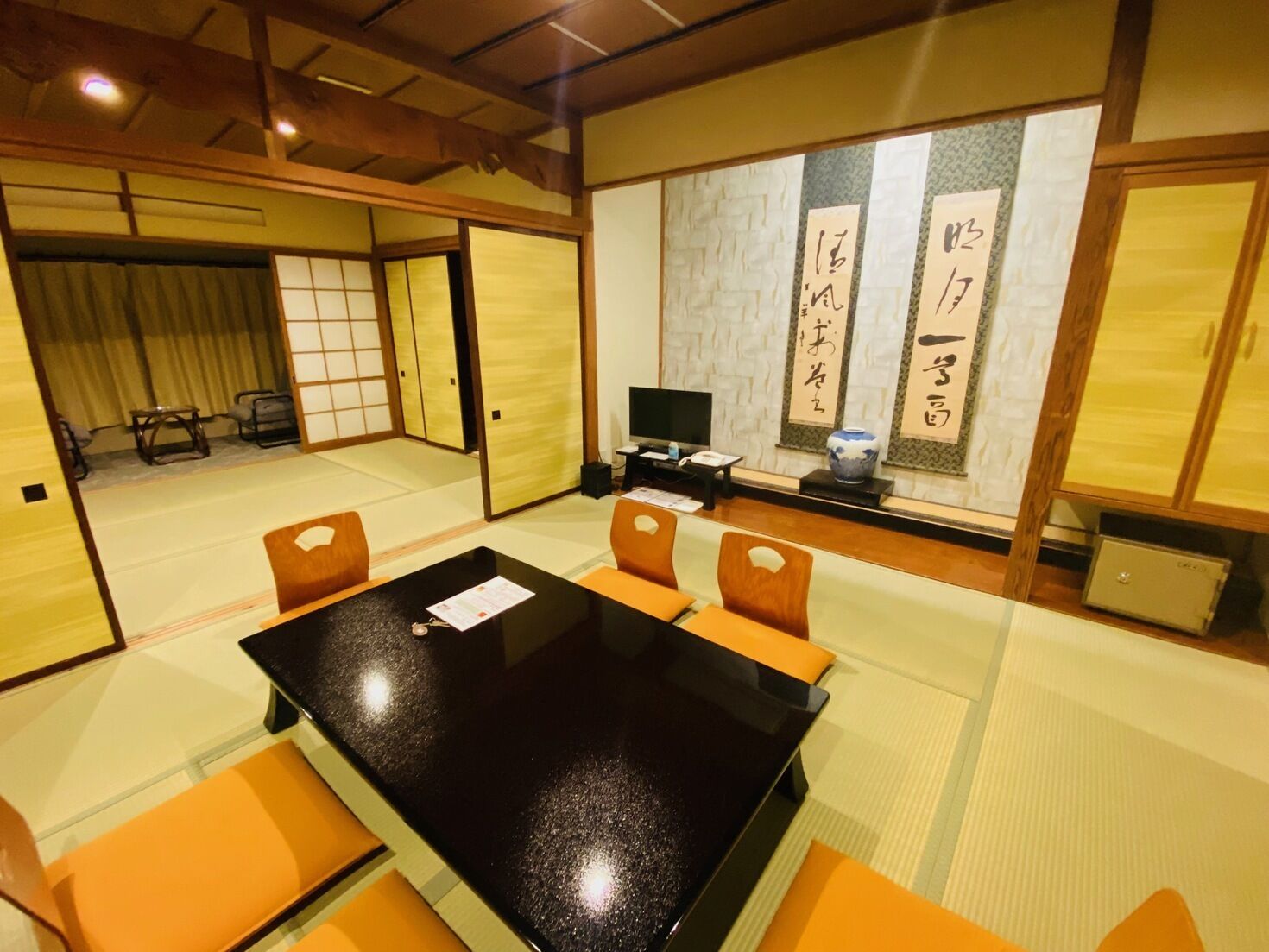 Een traditionele Japanse kamer met tatami vloeren, een zwarte tafel en oranje kussens.