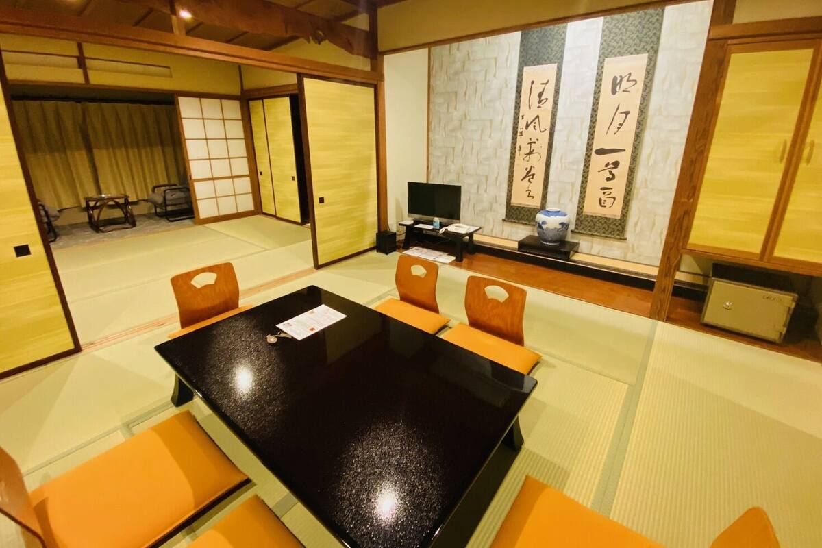 A traditional Japanese-style room with tatami flooring, a black table, and orange cushions.