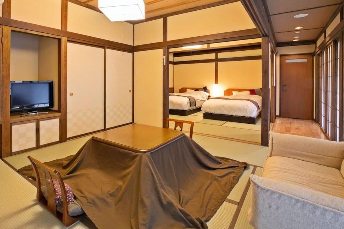 A traditional Japanese-style room with tatami flooring, a television, a sofa, and a bed.