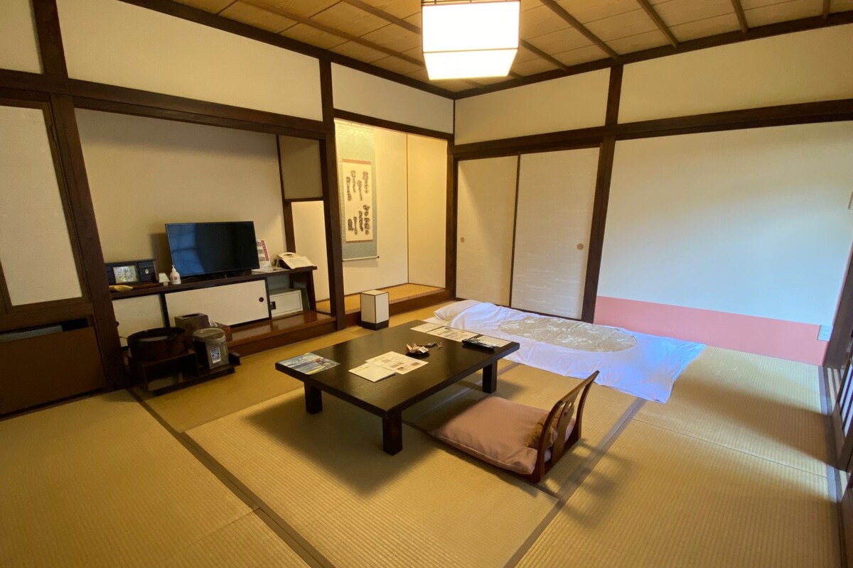 A traditional Japanese room with tatami flooring, a low table with cushions, a television, and a sliding door.