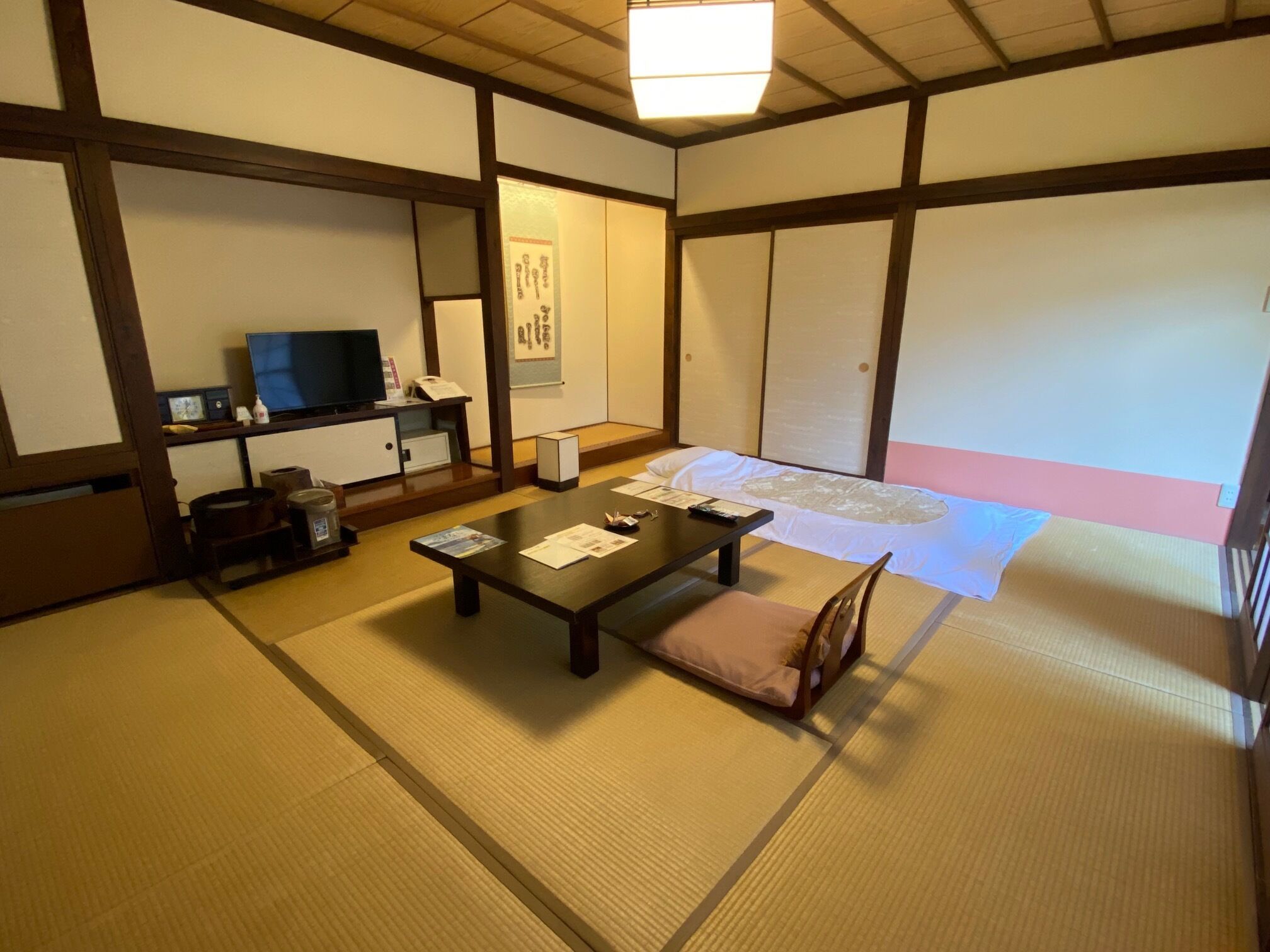 Een traditionele Japanse kamer met tatami vloerbedekking, een lage tafel, een televisietoestel en een schuifdeur.