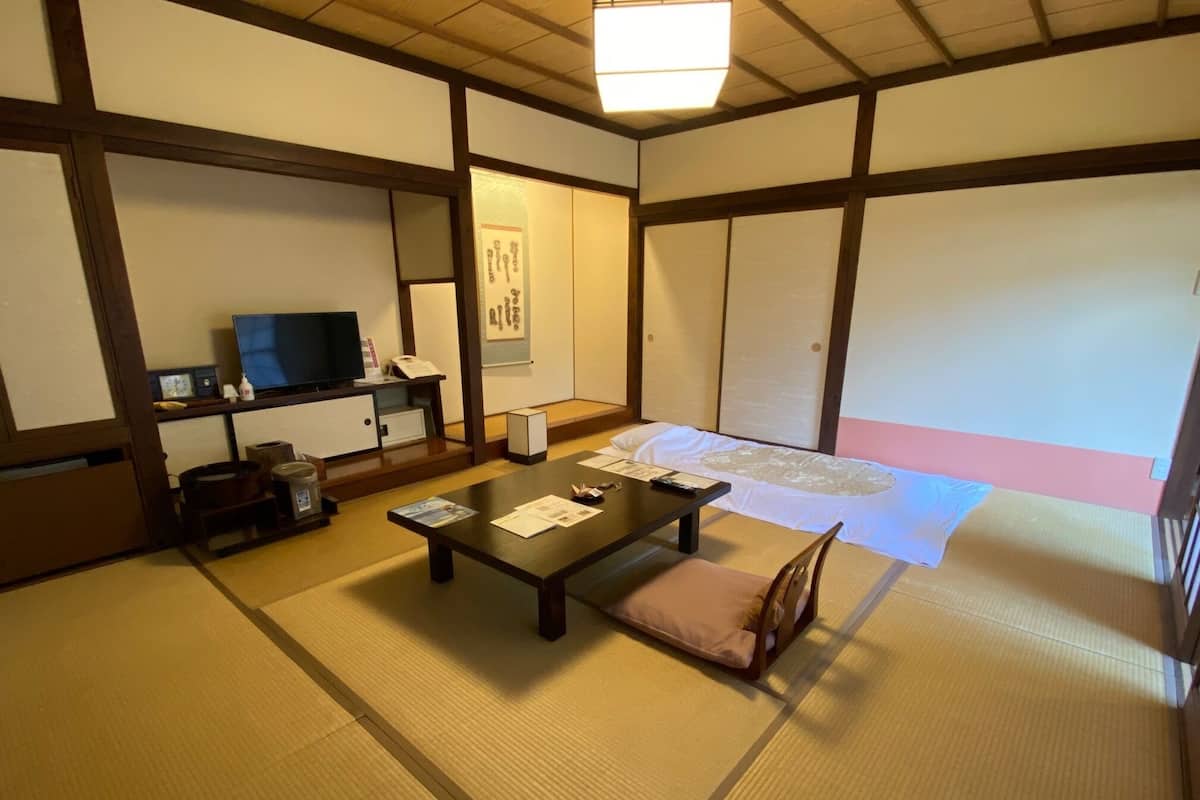 A traditional Japanese room with tatami flooring, a low table with cushions, a television, and a sliding door.