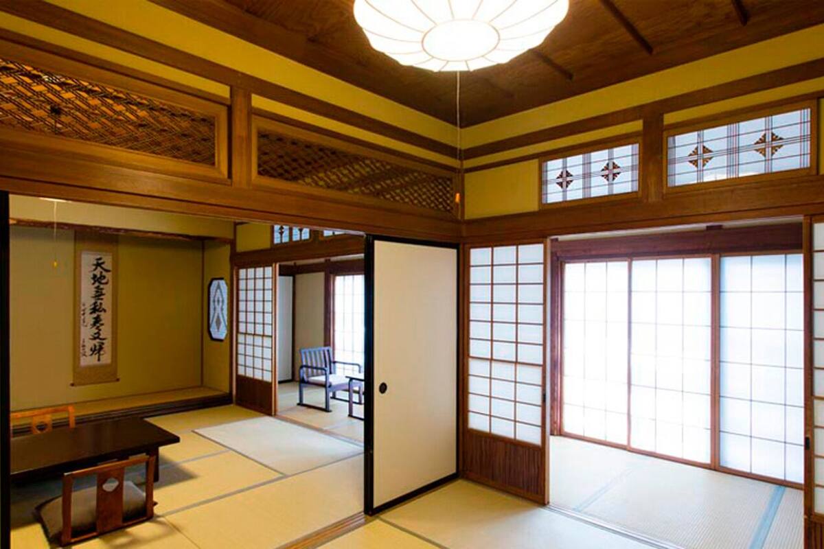 A traditional Japanese room with tatami flooring, sliding doors, and a low ceiling with a hanging light fixture.