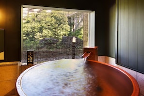 A hot tub with a view of a forest through a window.