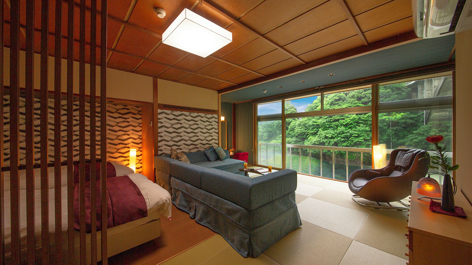 A modern room with a sofa, a massage chair, a large window with a view of greenery, and a ceiling light.