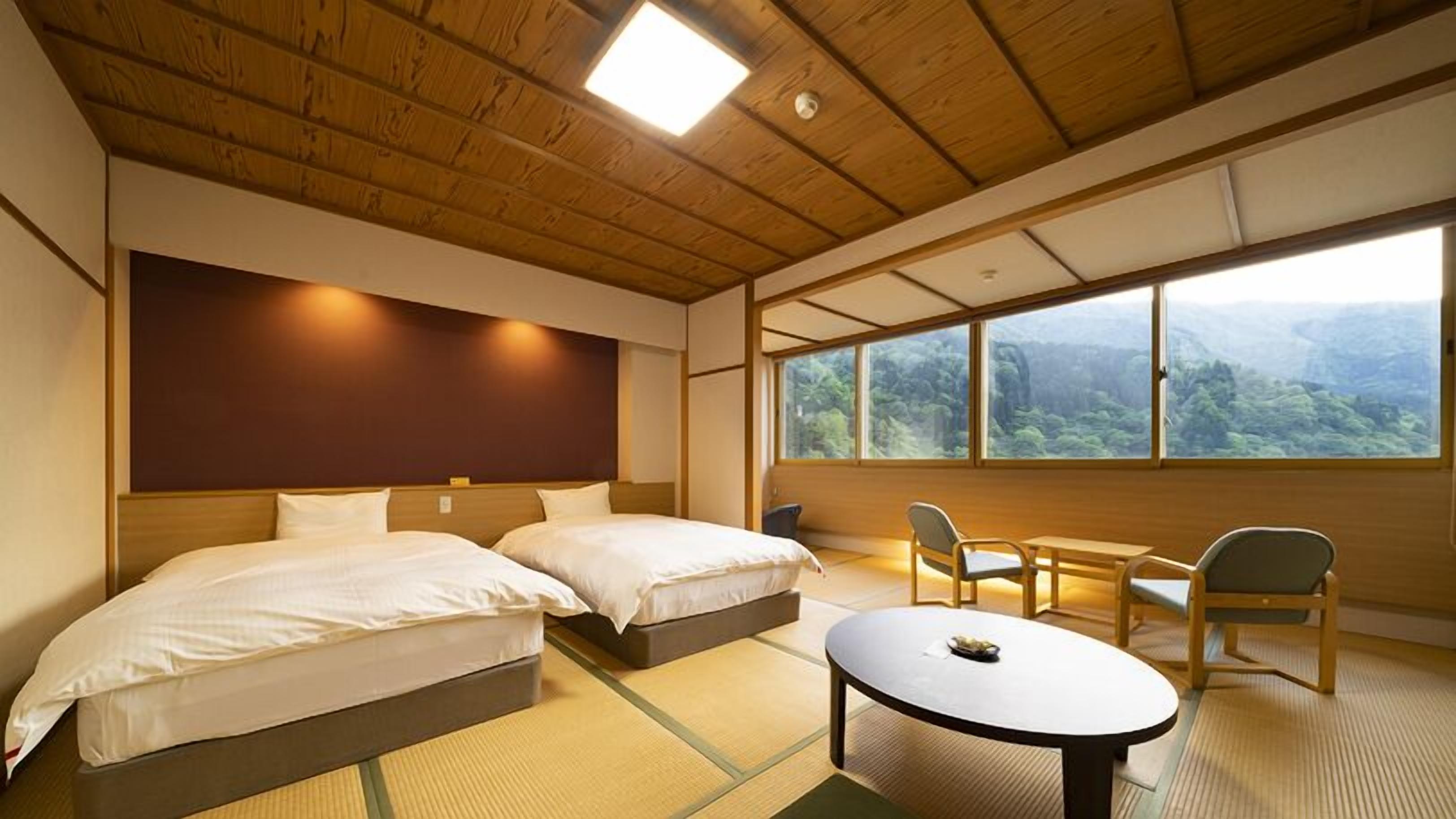 Ein Zimmer mit zwei Betten, einem kleinen Tisch, Stühlen und einem großen Fenster mit Blick auf einen Wald.