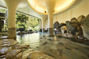 Un área de spa con grandes formaciones rocosas, un sendero de piedra y vistas a la vegetación a través de amplias ventanas.
