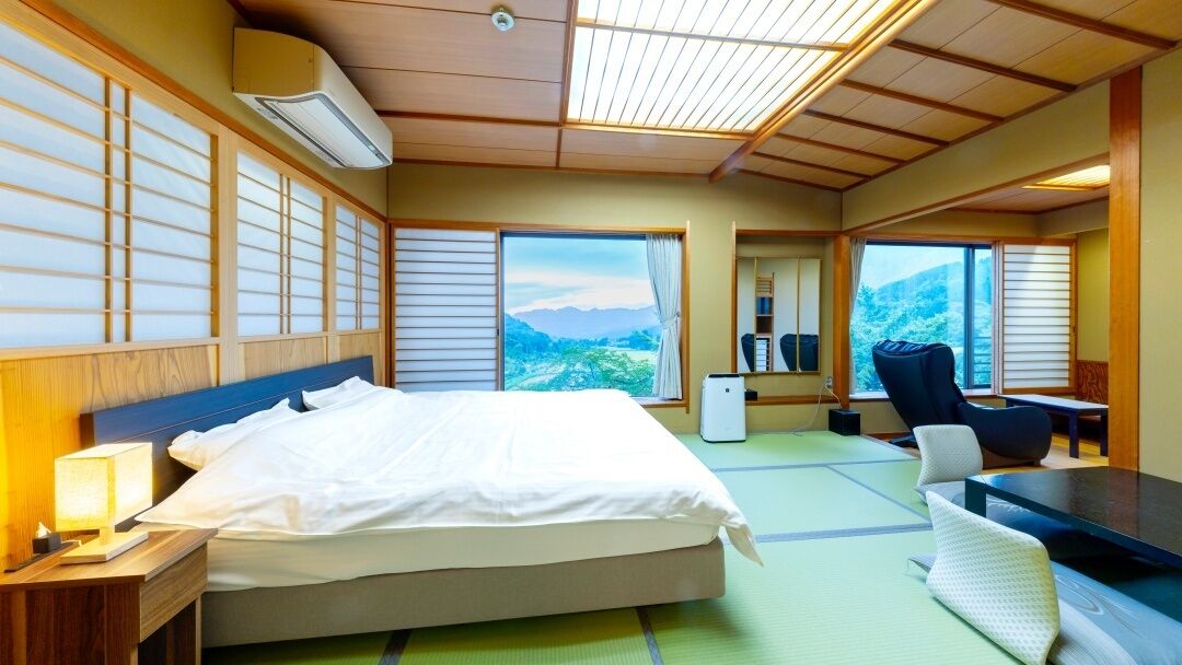 Una habitación de hotel con cama, escritorio, silla y ventanas amplias con vistas a la montaña.