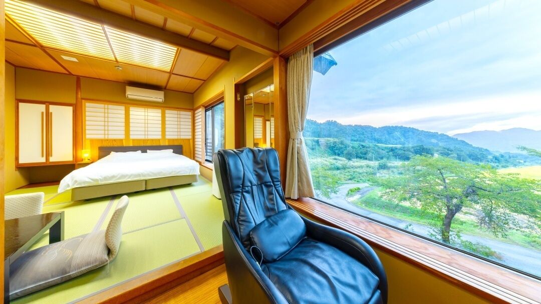 Una habitación con una cama, una silla de masaje, un futón y vistas a un paisaje.
