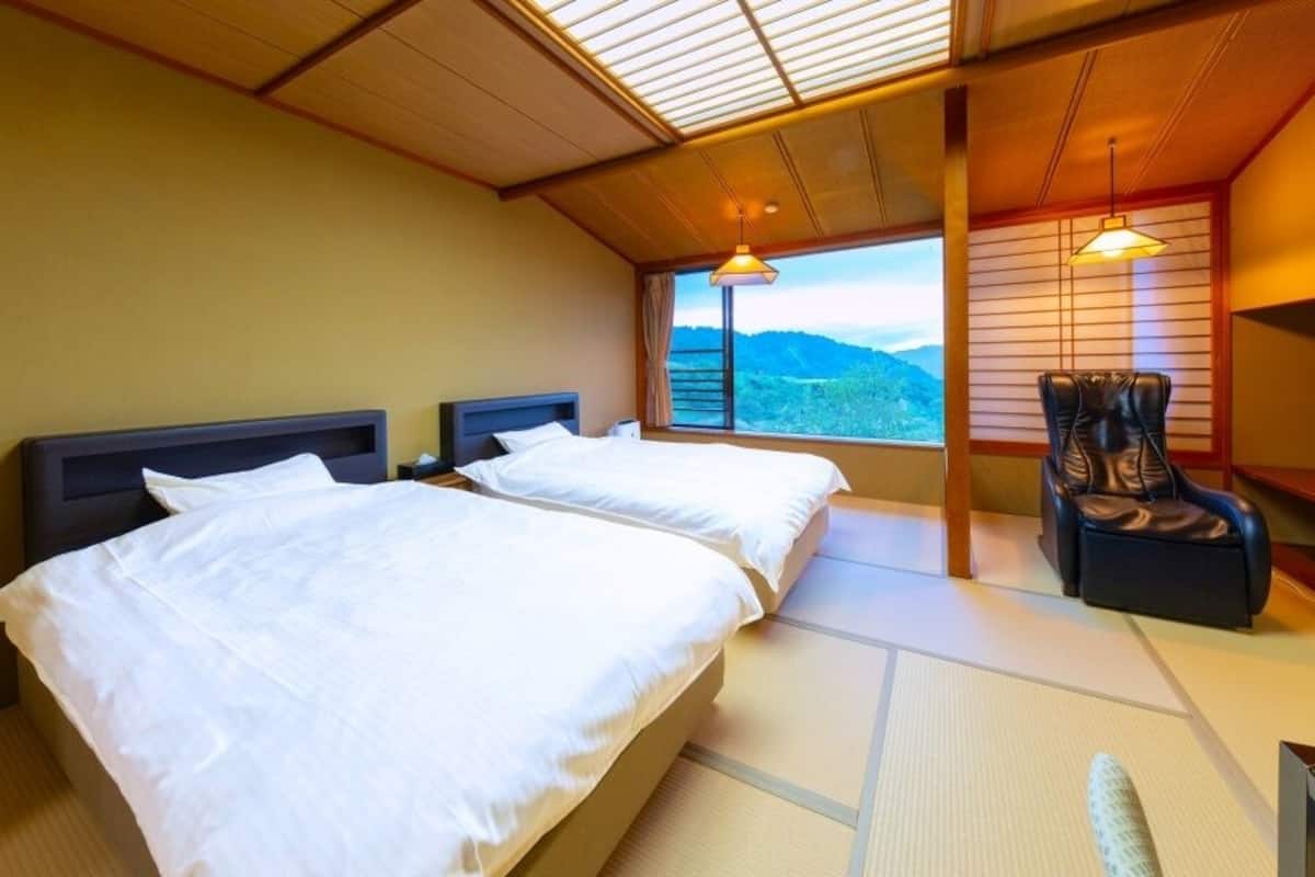 Hotellihuone, jossa on kaksi sänkyä, tuoli, näköala vuorille ja perinteinen japanilainen sisustus.