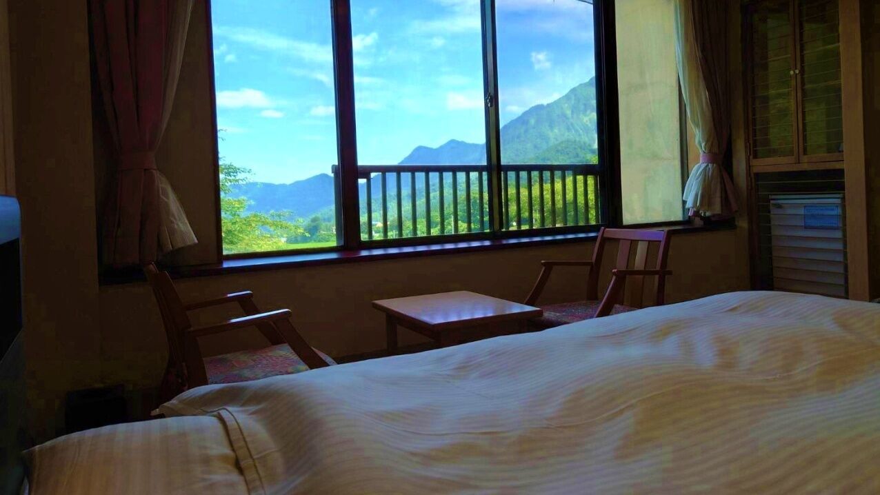 Una habitación con cama, una mesita, dos sillas y ventana con vista a las montañas.