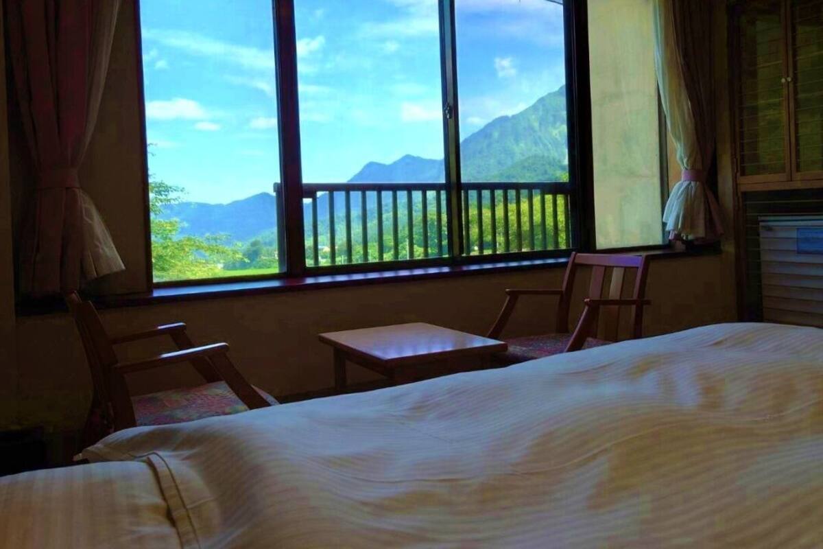 A room with a bed, a small table, two chairs, and a window with a view of mountains.