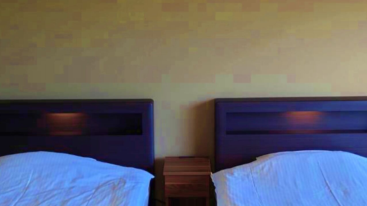 Dos camas individuales con cabeceros de madera, una mesita de noche de madera y una pared con un diseño pixelado.