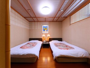 Habitación de hotel con dos camas individuales, una mesita de noche con lámparas, un cuadro enmarcado en la pared y piso de madera.