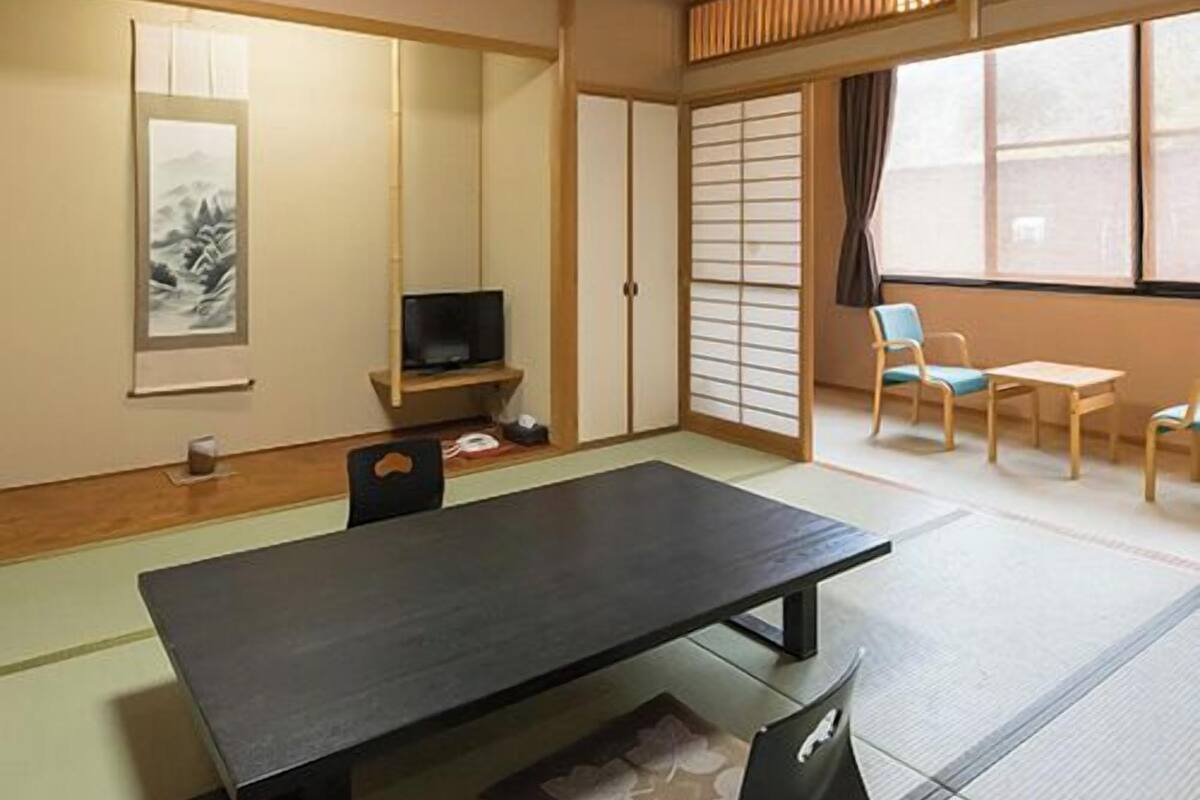 A traditional Japanese room with tatami flooring, a low table, a television, sliding doors, and a view through large windows.