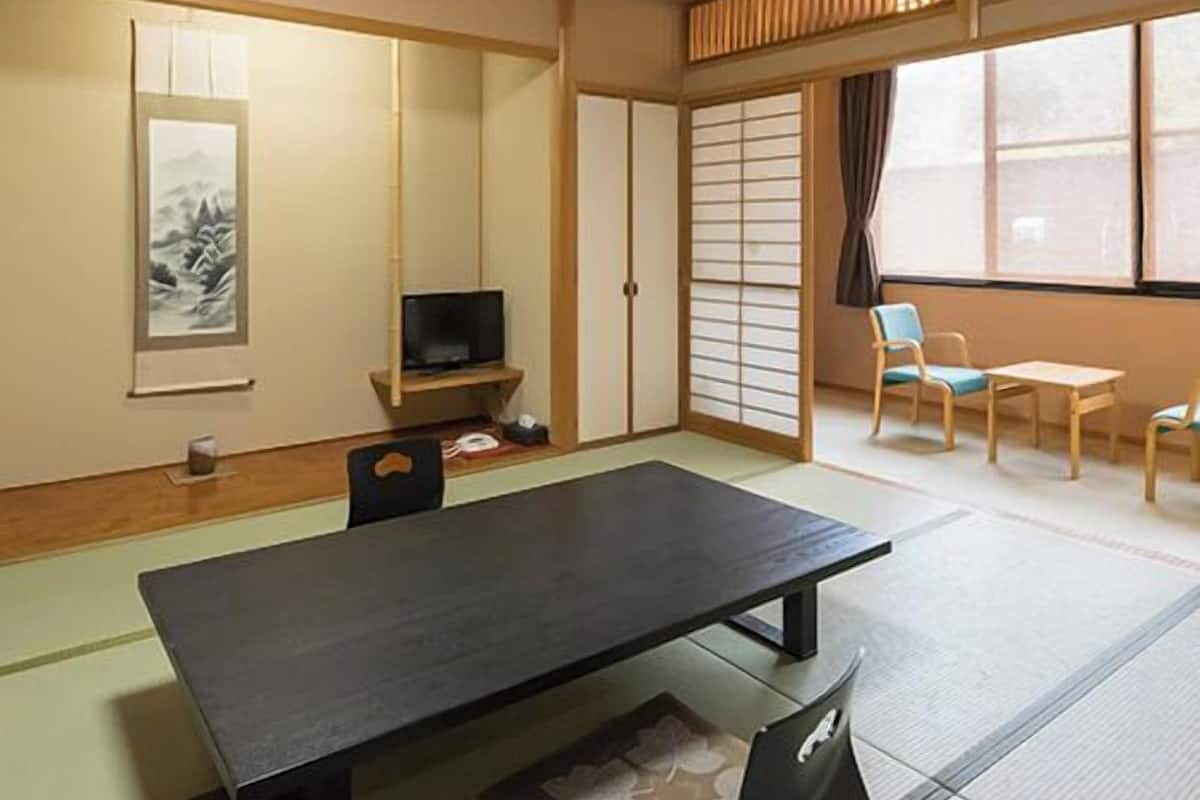 Ein traditioneller japanischer Raum mit Tatami-Böden, einem niedrigen Tisch, einem Fernseher, Schiebetüren und Blick durch große Fenster.