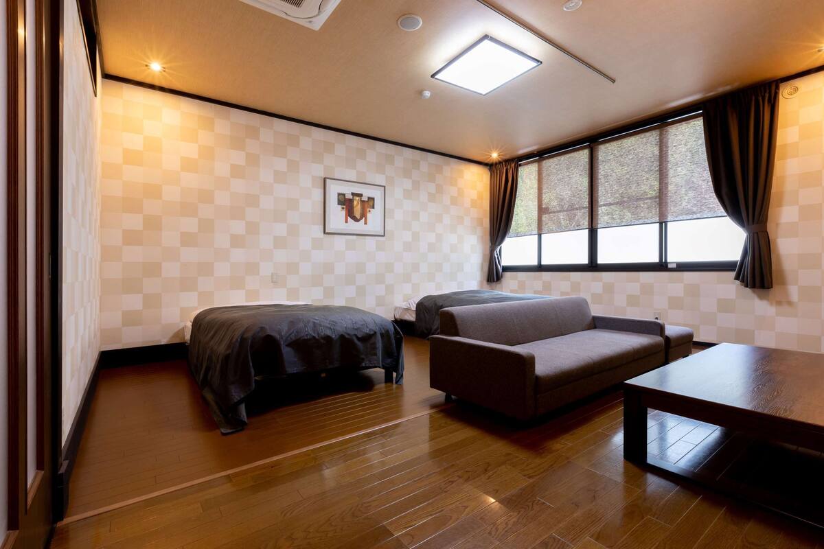 A room with two beds, a sofa, a coffee table, a window with curtains, and a checkered wall pattern.
