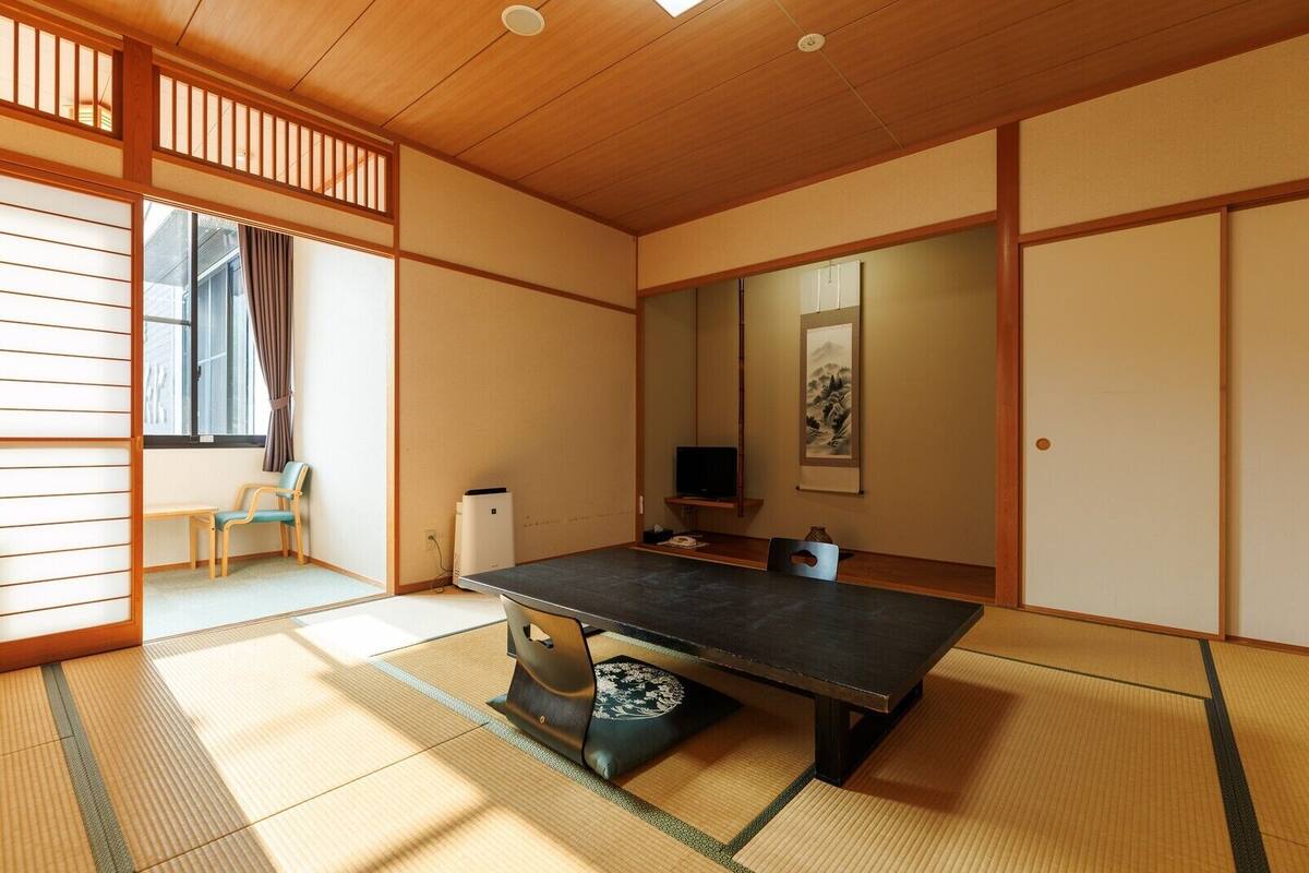 A traditional Japanese-style room with tatami flooring, a low table, a television, and a sliding door.