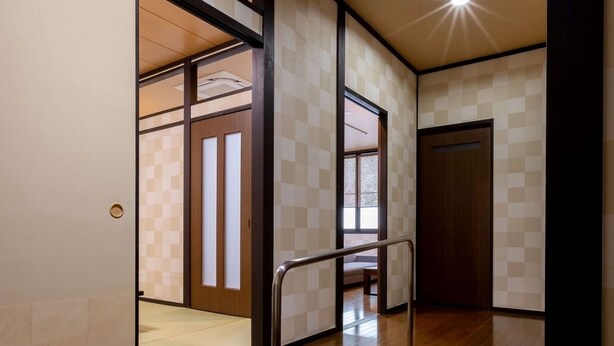 A hallway with wooden flooring, a metal handrail, and a checkered wall pattern. - Sugatani Onsen (Nagahama)