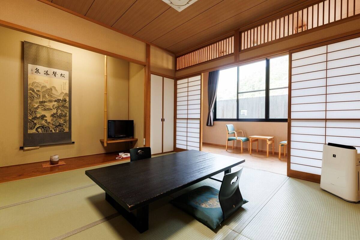 A traditional Japanese room with tatami flooring, a low table, a television, sliding doors, and a large window.