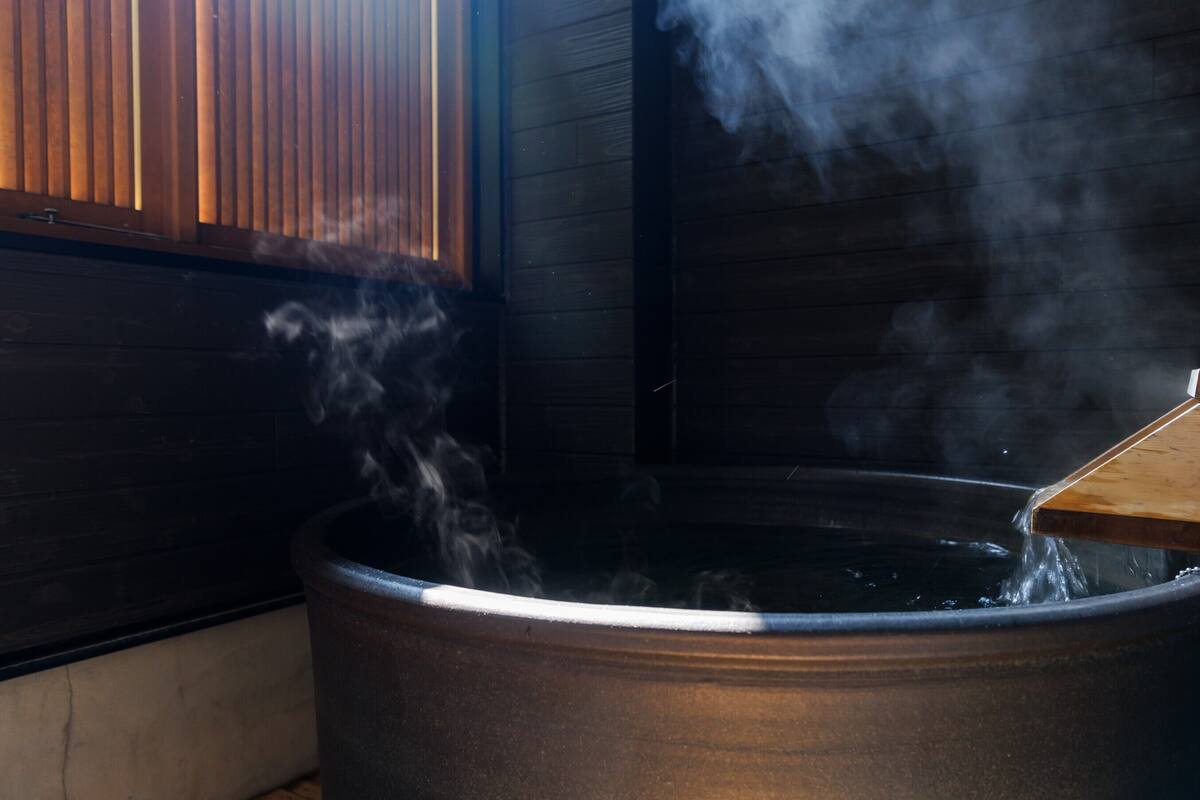 A hot tub with steam rising, surrounded by wooden walls and a window.