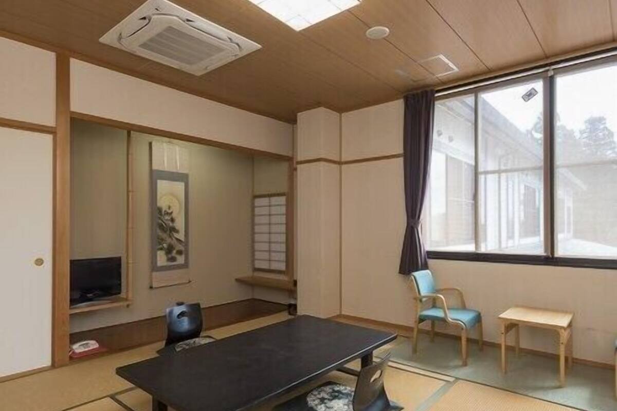A traditional Japanese room with tatami flooring, a tatami mat table, a television, a window with curtains, and a sliding door.