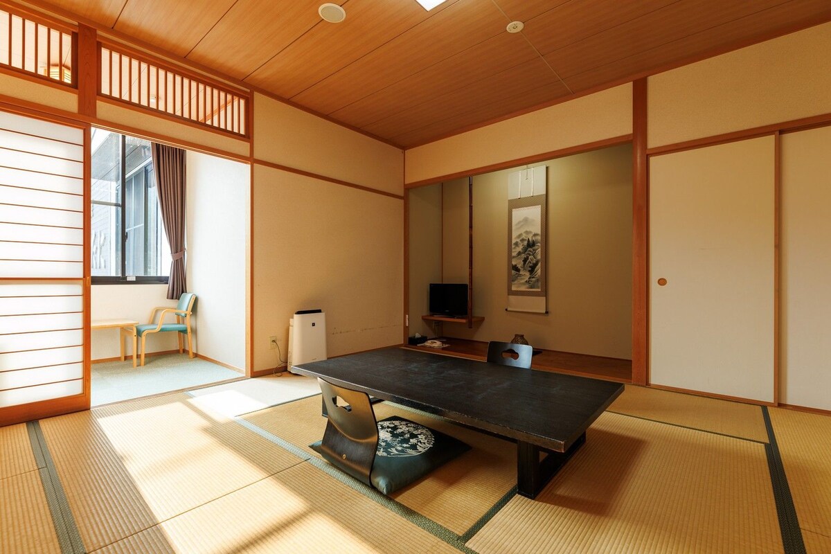 A traditional Japanese-style room with tatami flooring, a low table, a television, and a sliding door.
