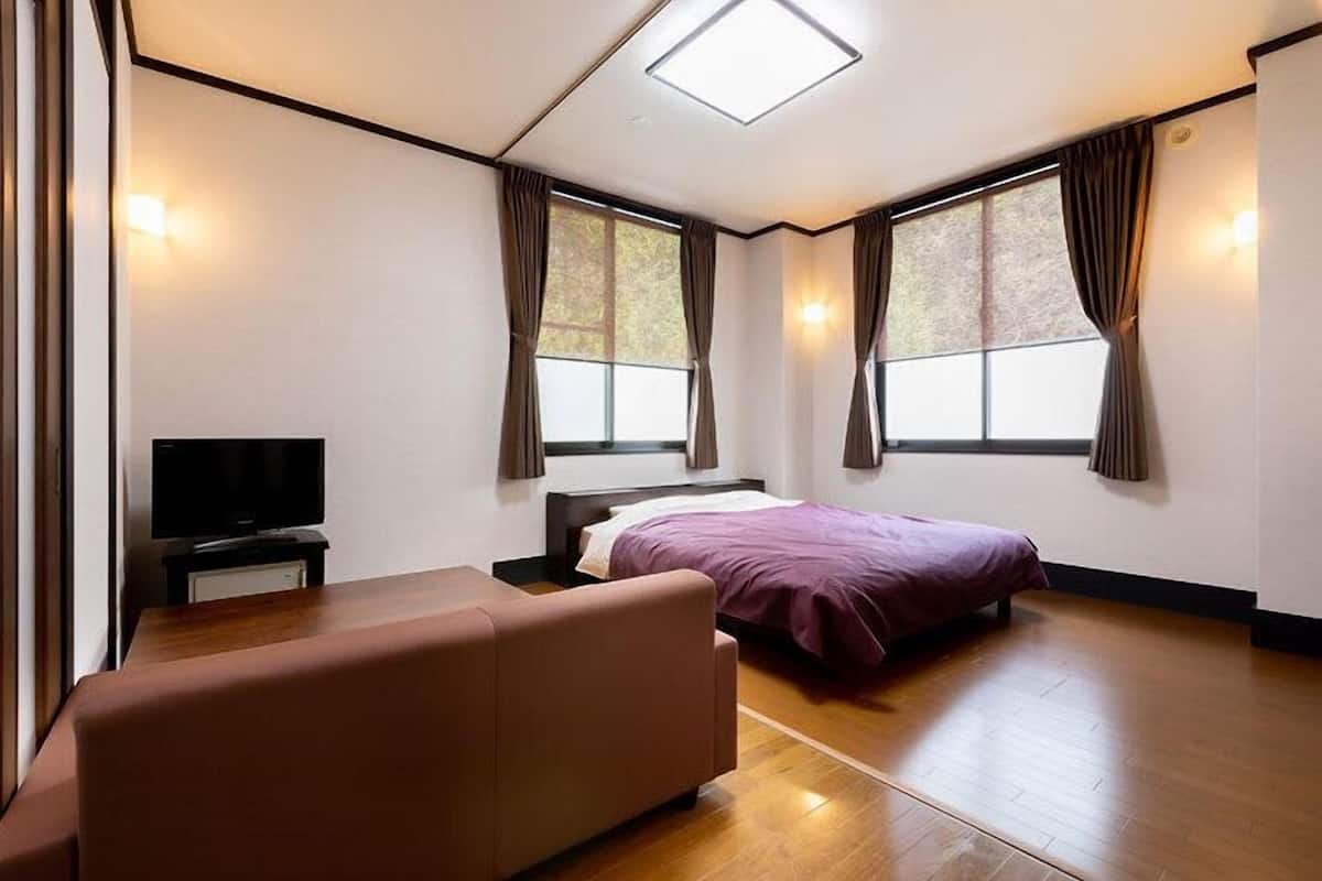 A bedroom with a bed, a sofa, a TV, and large windows.