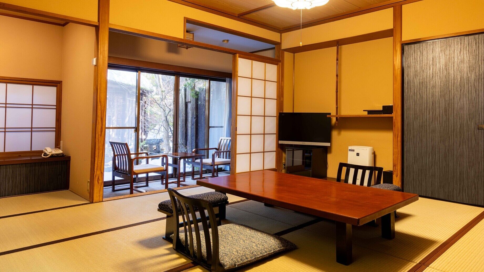 Ein traditioneller japanischer Raum mit Tatami-Böden, einem niedrigen Tisch, Stühlen, einem Fernseher und Schiebetüren.