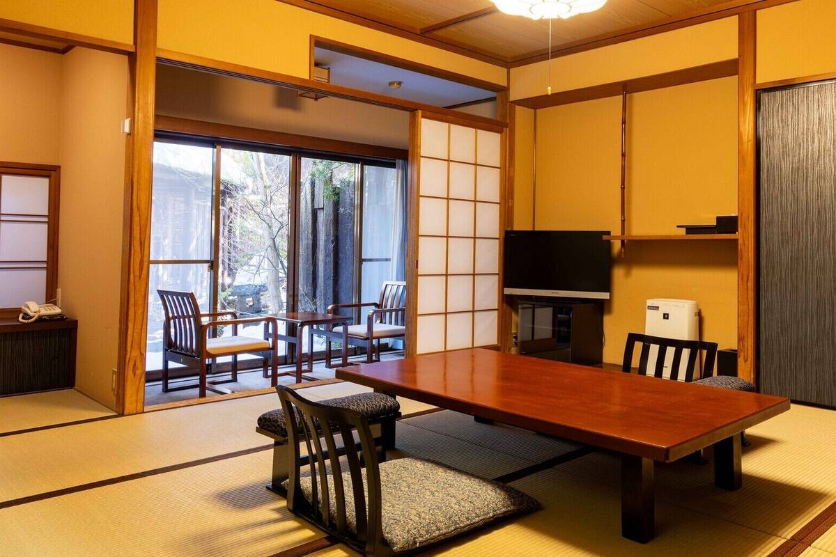 A traditional Japanese room with tatami flooring, a low table, chairs, a television, and sliding doors.