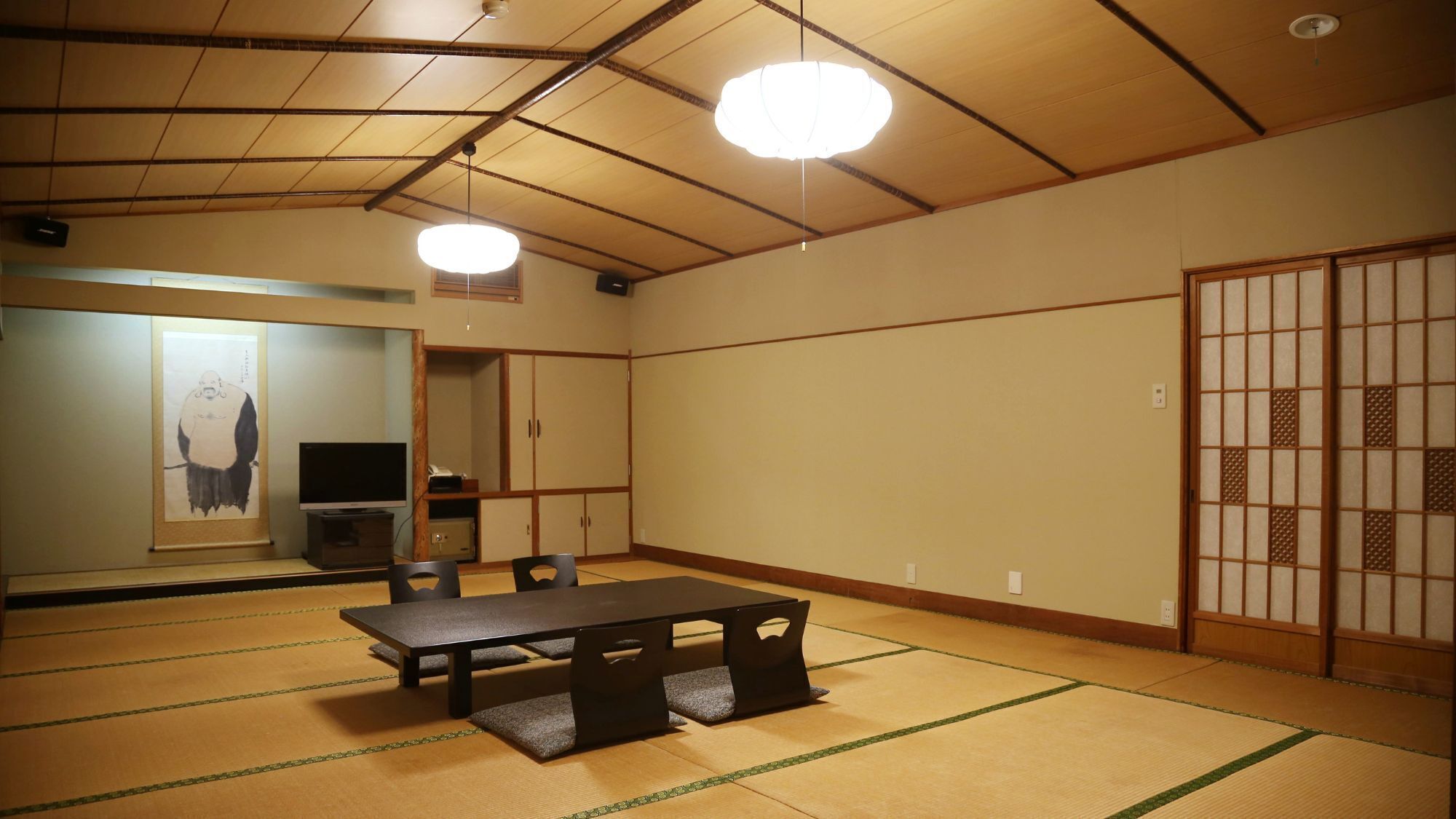 A traditional Japanese room with tatami flooring, a tatami mat table, a television, and a shoji screen.