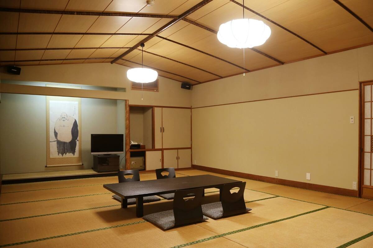 A traditional Japanese room with tatami flooring, a tatami mat table, a television, and a shoji screen.