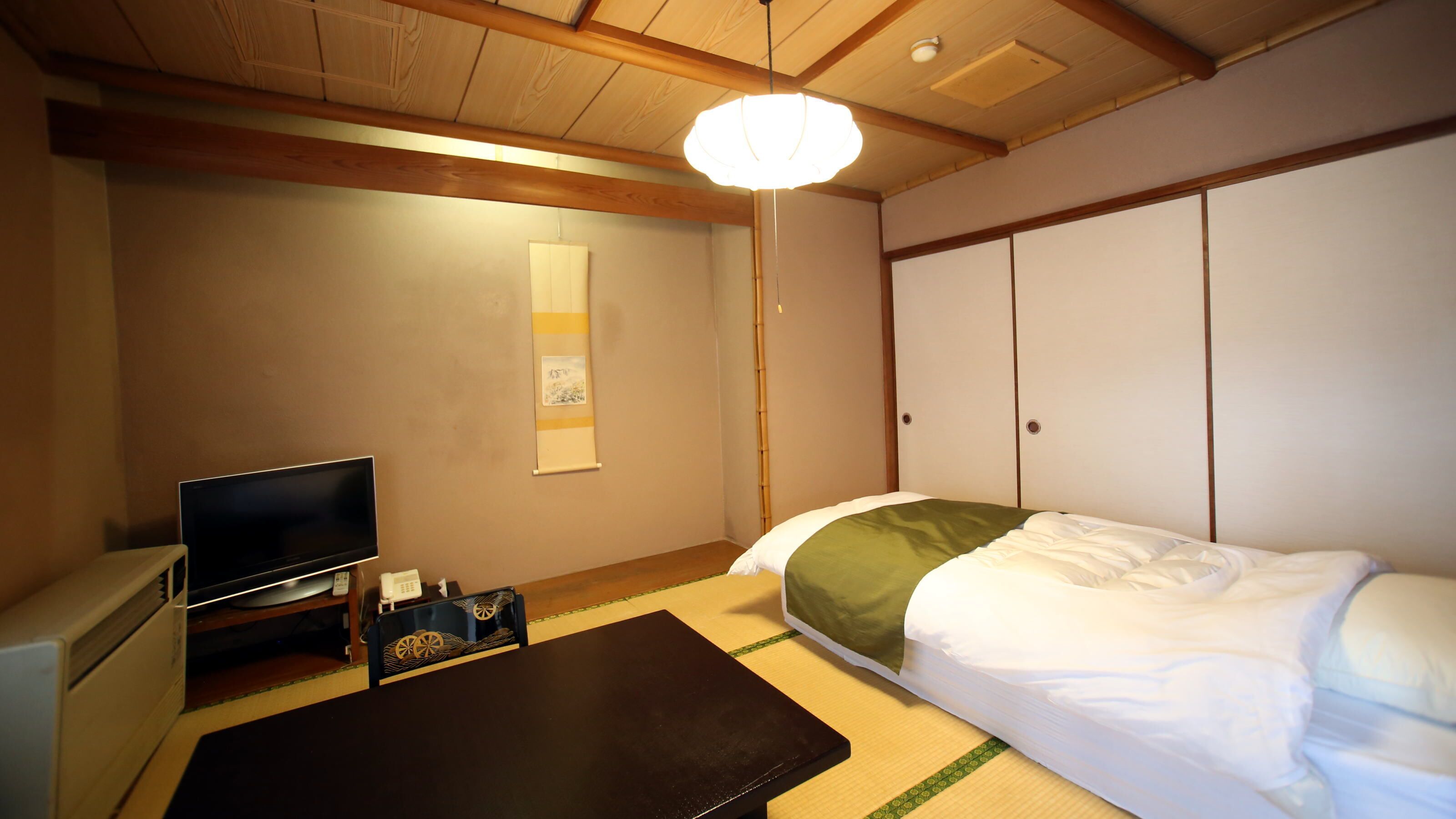 Ein Zimmer mit einem Bett, einem Fernseher, einem Schreibtisch und einer traditionellen japanischen Schiebetür.
