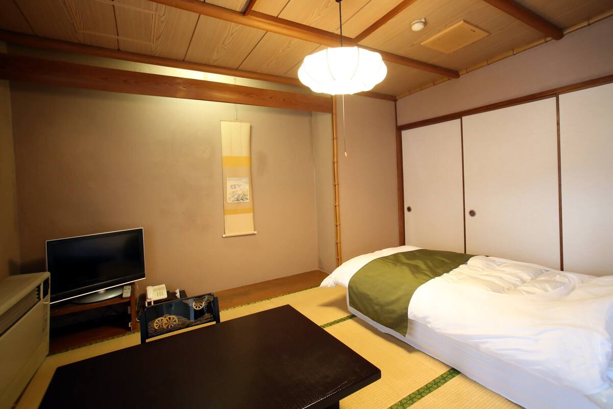 A room with a bed, a television, a desk, and a traditional Japanese sliding door.