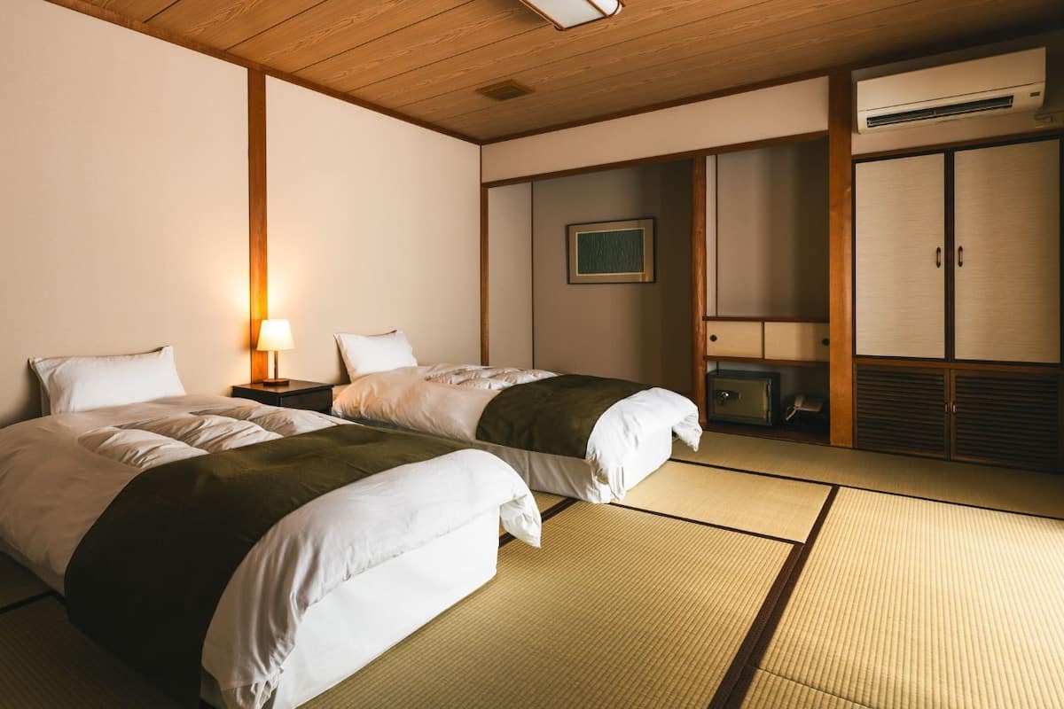 A hotel room with two beds, a bedside table with a lamp, a wardrobe, and a framed picture on the wall.