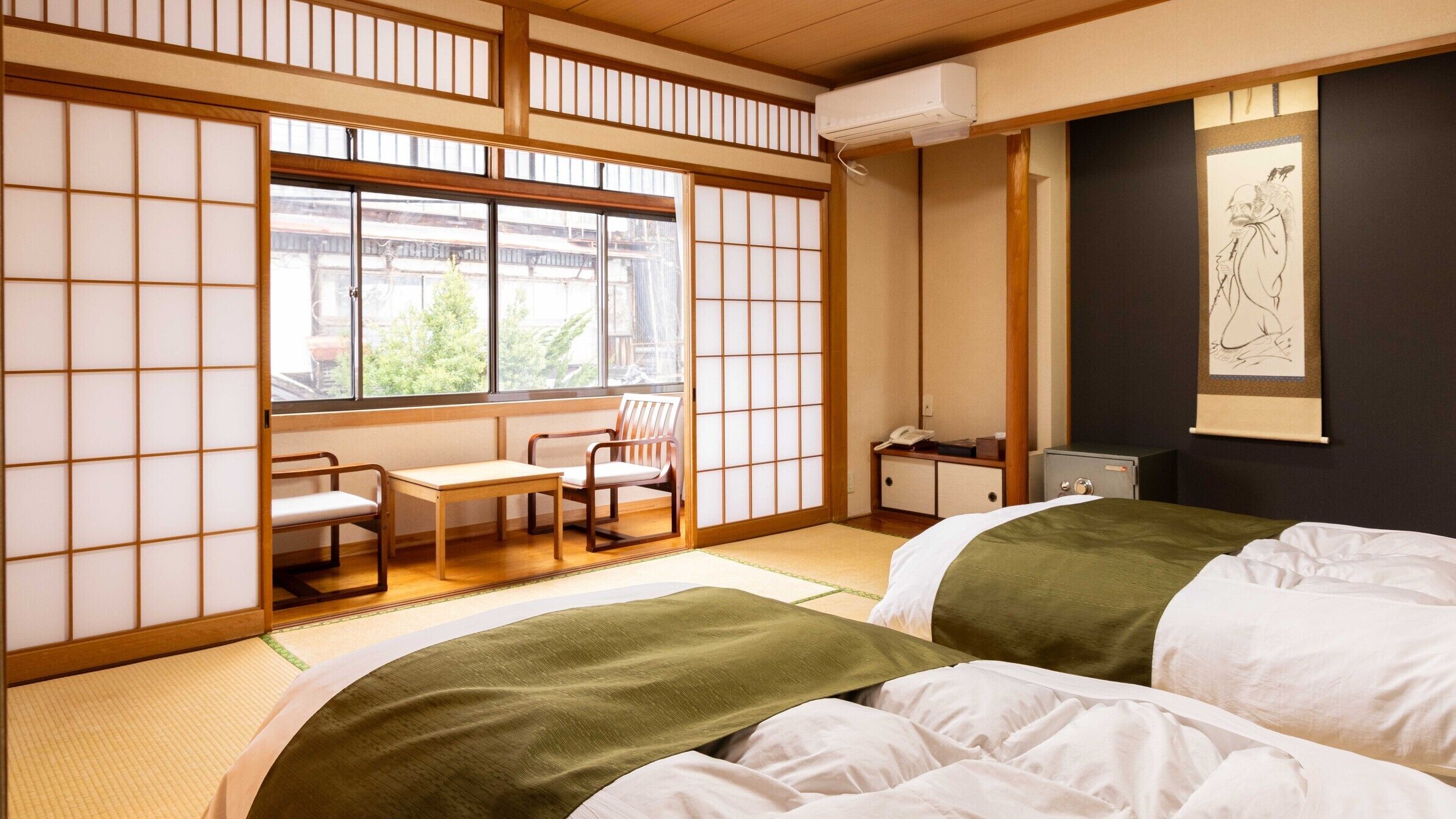 Ein traditioneller japanischer Raum mit Tatami-Boden, einem Futonbett, einem Schreibtisch mit Stühlen und einer verschiebbaren Shoji-Schirmwand.