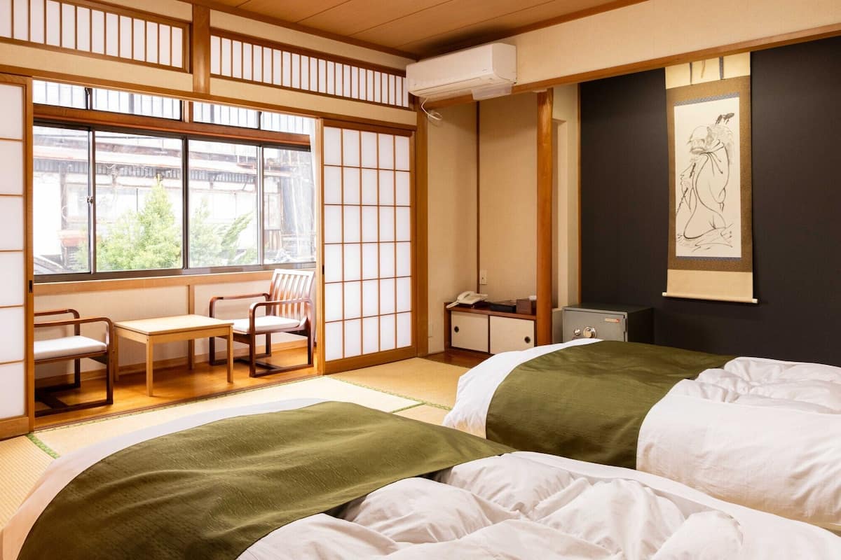 A traditional Japanese-style room with tatami flooring, a futon bed, a desk with chairs, and a sliding shoji screen.
