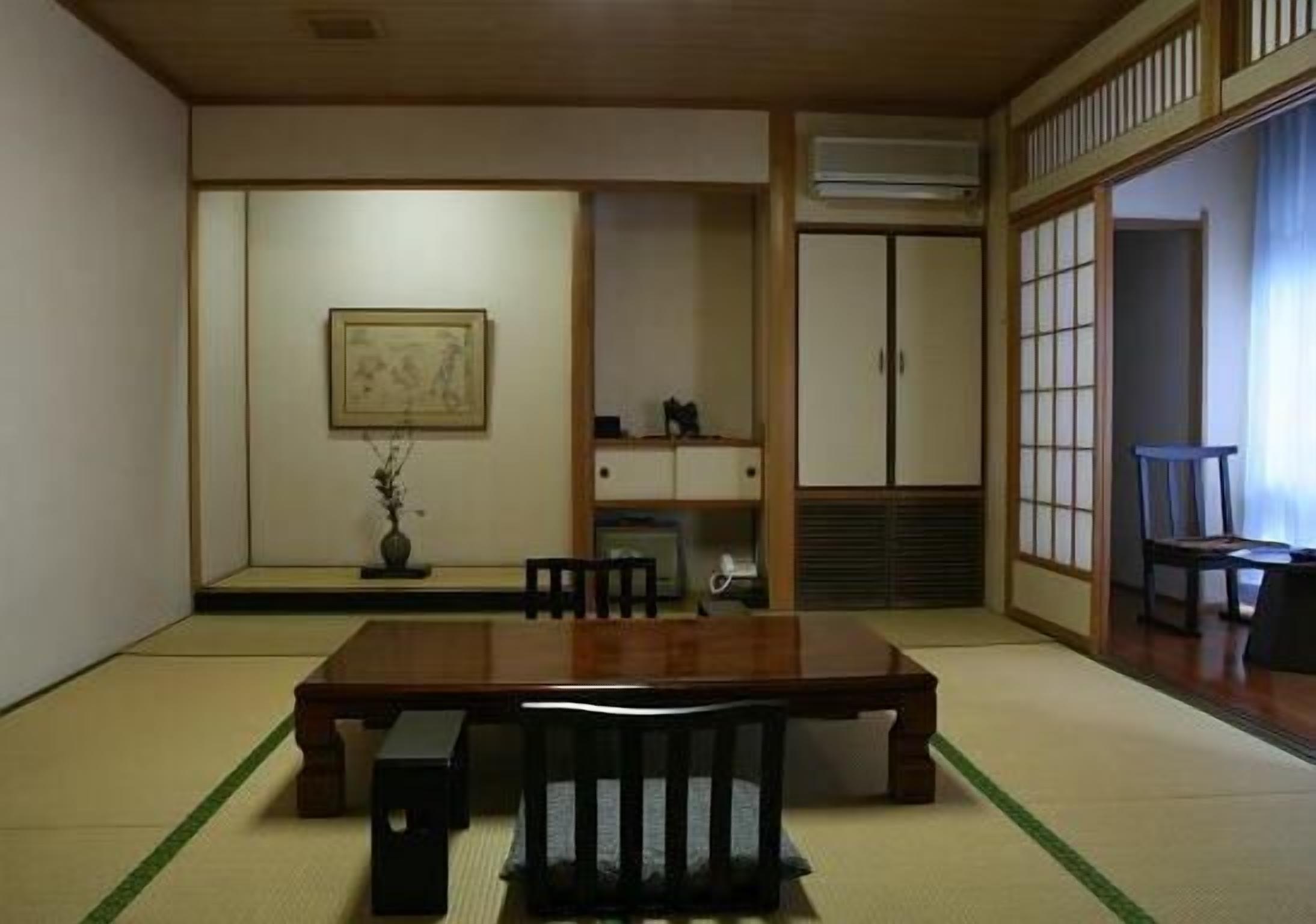 A traditional Japanese room with tatami flooring, a wooden table, chairs, a framed picture, and sliding doors.