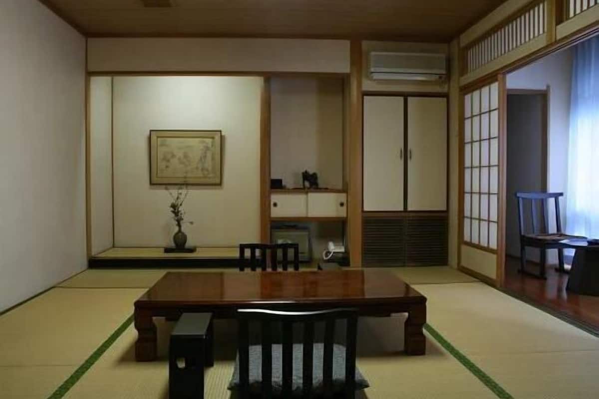 A traditional Japanese room with tatami flooring, a wooden table, chairs, a framed picture, and sliding doors.