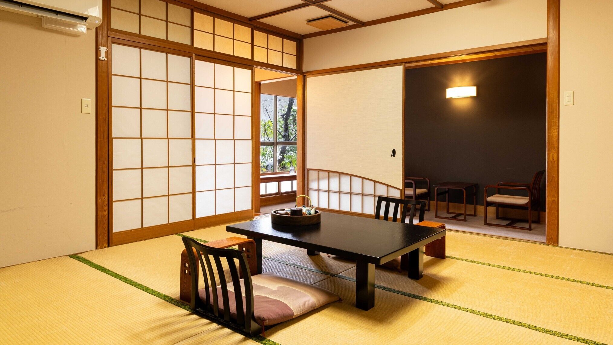 Ein traditioneller japanischer Raum mit Tatami-Bodenbelag, einem niedrigen Tisch mit Stühlen und Schiebetüren.