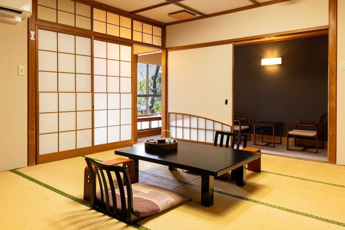 A traditional Japanese room with tatami flooring, a low table with chairs, and sliding doors.
