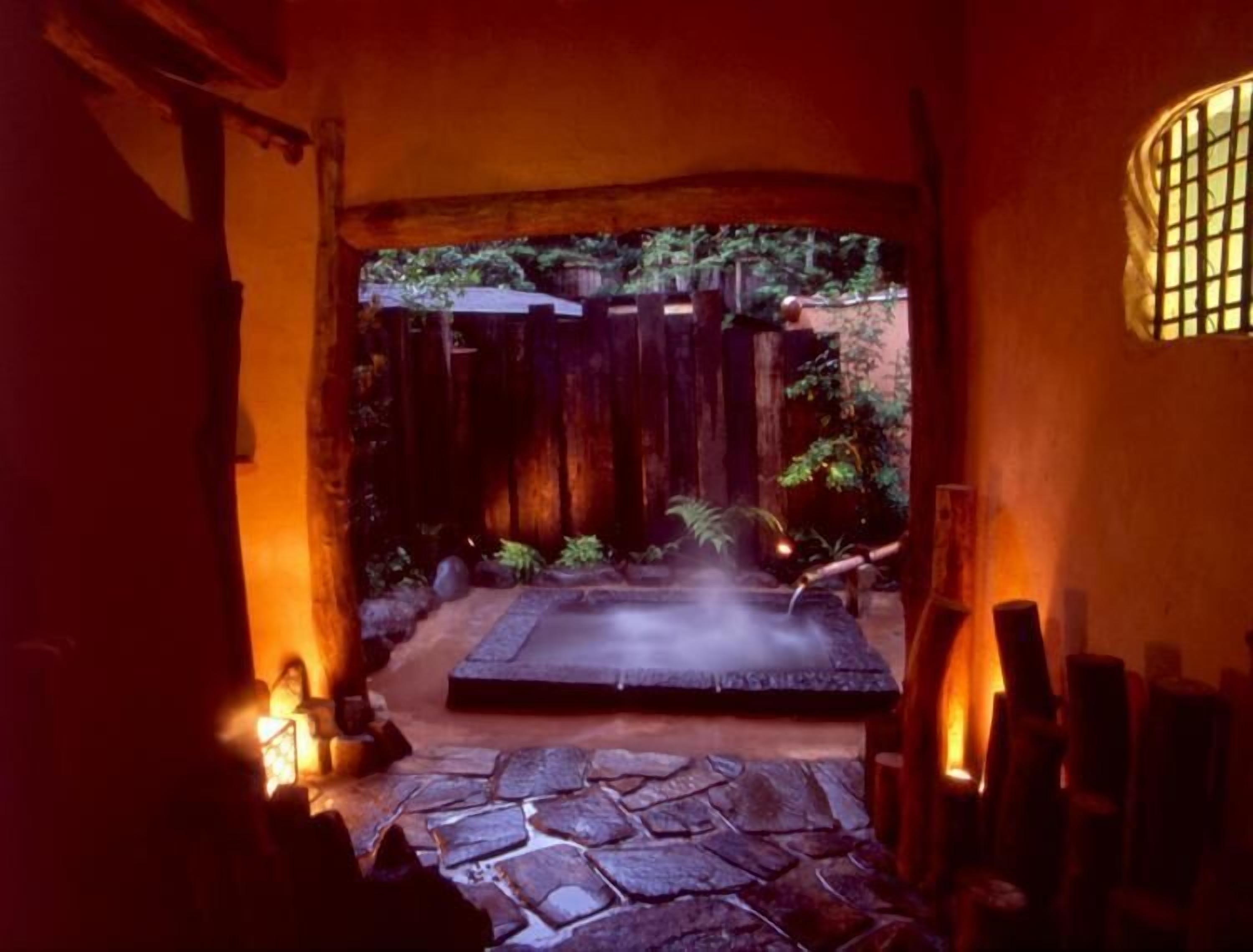 A stone pathway leading to a hot spring area with a wooden fence and greenery in the background.