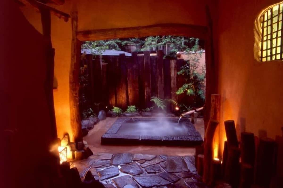 A stone pathway leading to a hot spring area with a wooden fence and greenery in the background.