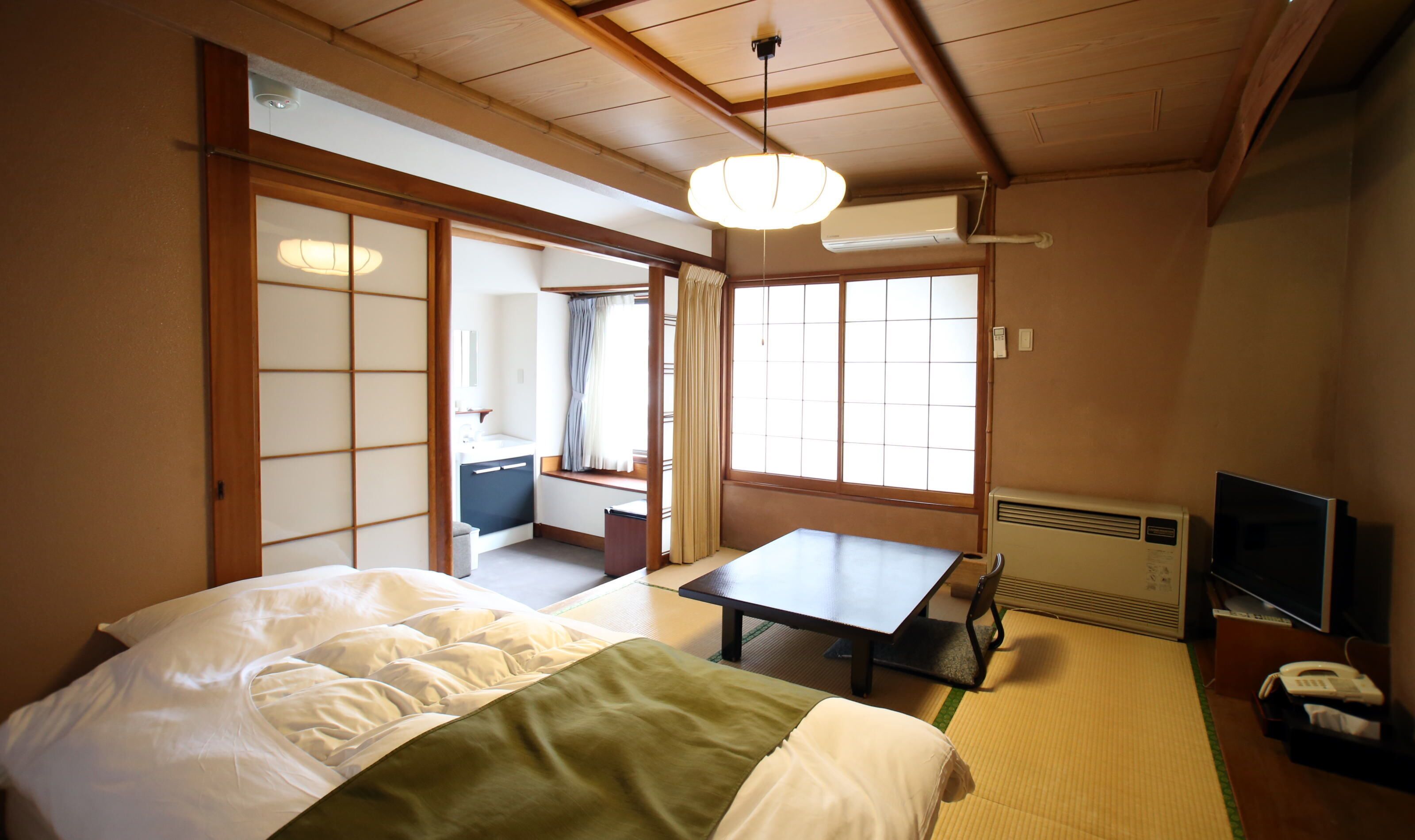 A traditional Japanese room with tatami flooring, a bed with a green and white bedspread, a table, and a television.