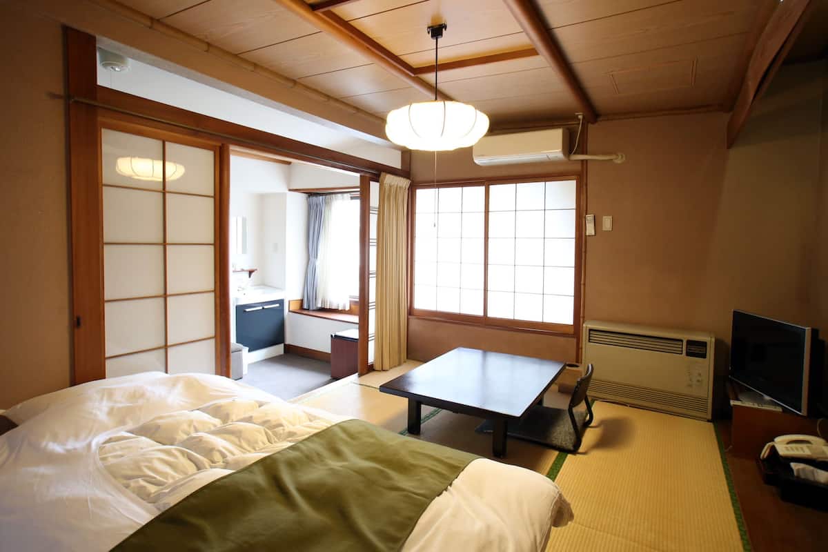 A traditional Japanese room with tatami flooring, a bed with a green and white bedspread, a table, and a television.