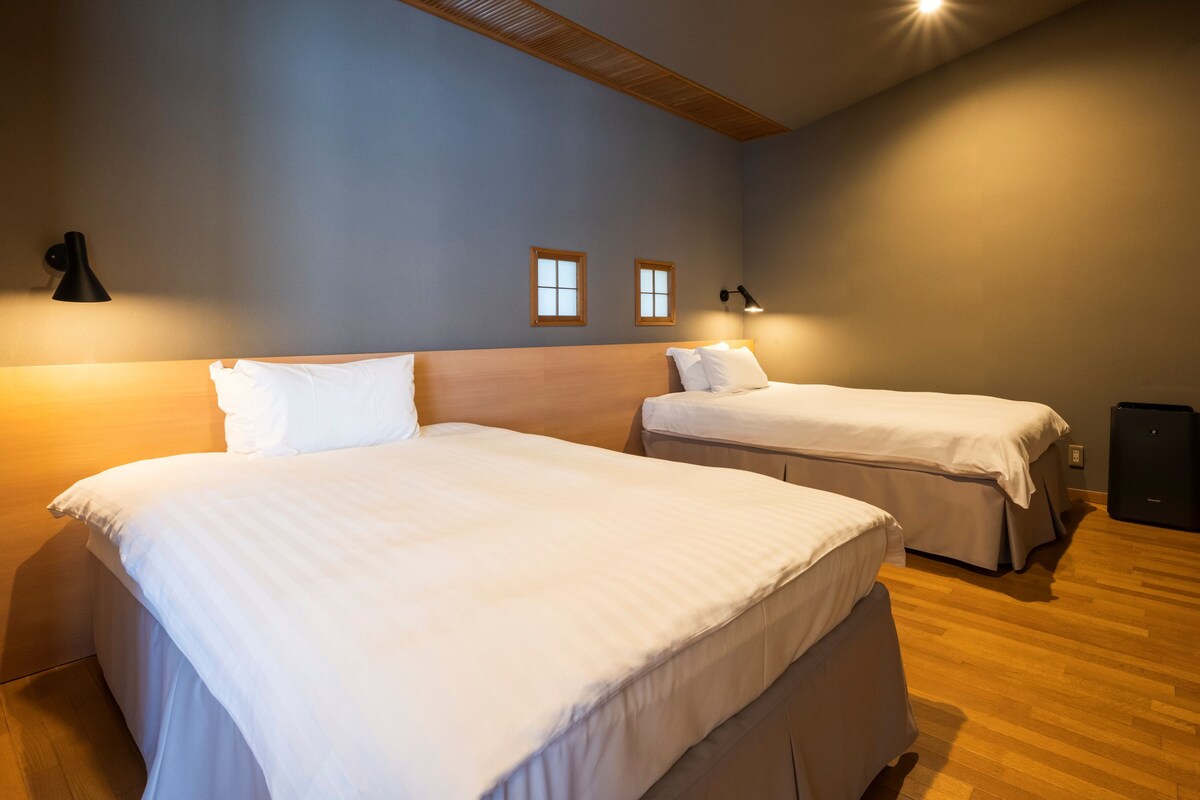 Habitación de hotel con dos camas, techo de madera, televisor de pared y un altavoz pequeño.