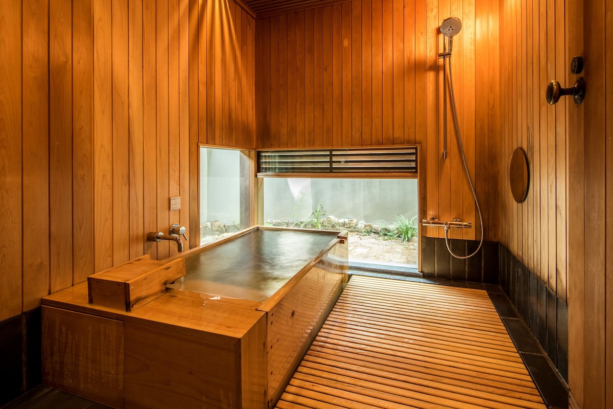 Un sauna de madera con banco, ducha y vista al exterior a la vegetación.