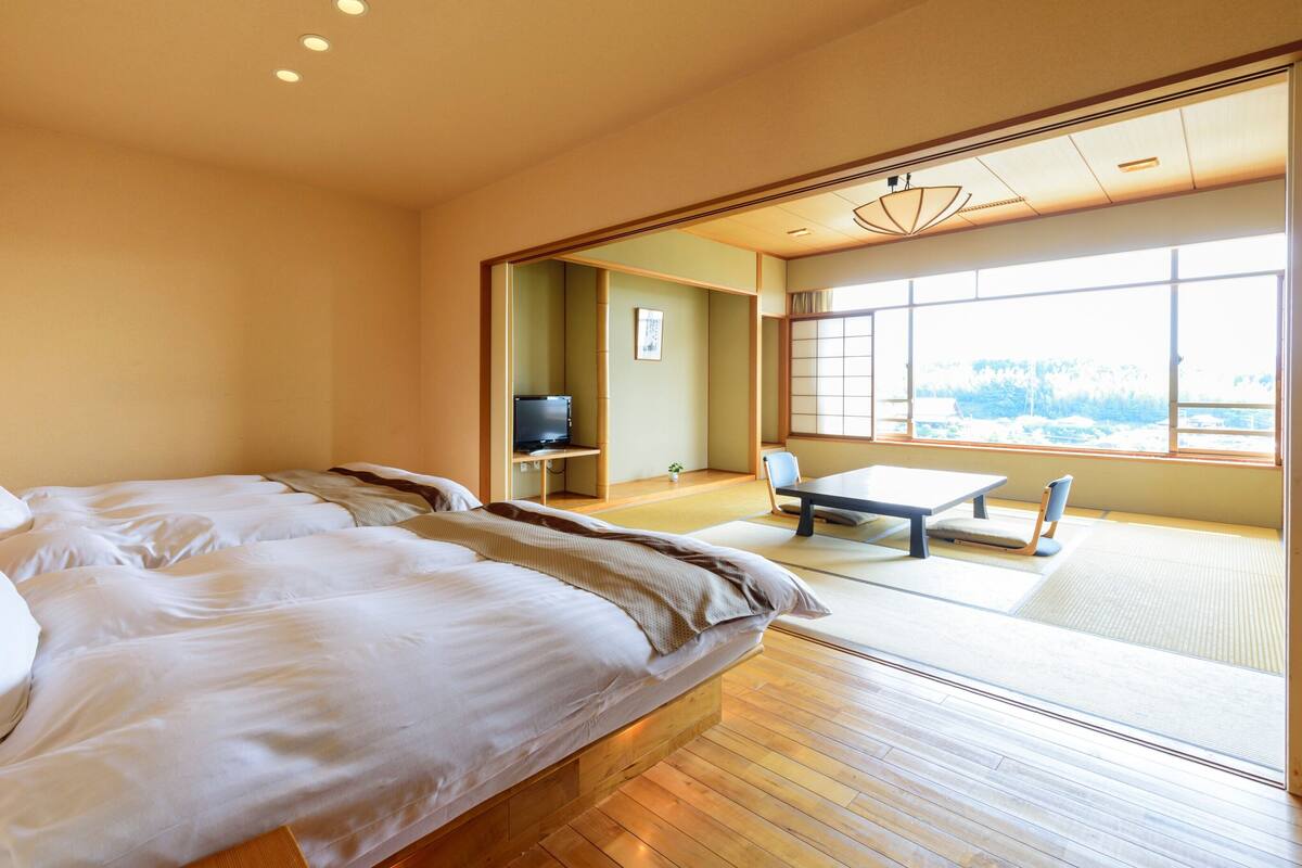 A hotel room with a bed, a television, a tatami mat area, and a view of the outdoors.